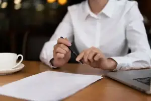 A close-up of a professional paralegal reviewing documents at a desk, with a laptop and a cup of coffee nearby.